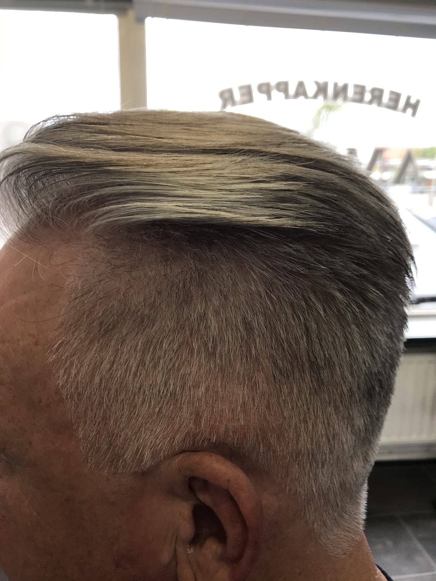 Grijs haar met kort geknipte zijkanten en een zijwaarts gekamde bovenkant, voor het raam van de zaak